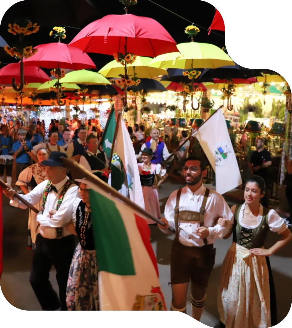 Público em desfile de festa típica sob guarda-chuvas coloridos